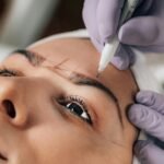 A beautician performs precise microblading on a client's eyebrows in a salon.